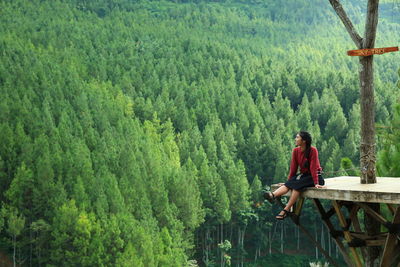 Young woman sitting against trees at forest