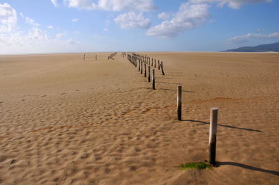 Wooden posts on sand at beach against sky