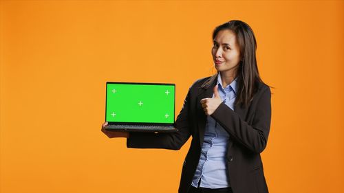 Portrait of young businesswoman using digital tablet against yellow background