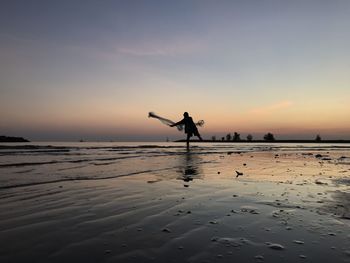 Silhouette man standing on beach against sky during sunset