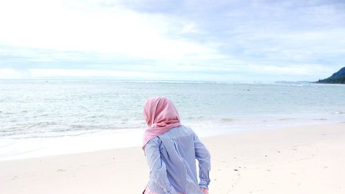 Rear view of woman standing on beach against sky