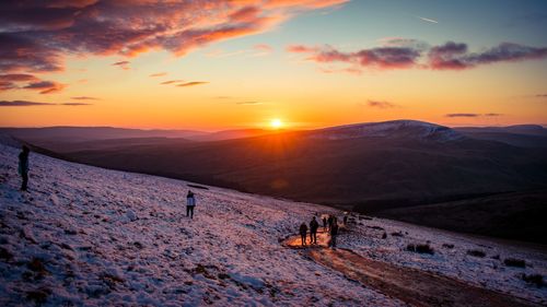 People on snowcapped mountain against sky during sunset