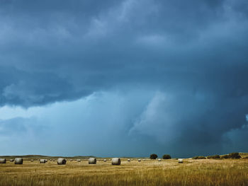 Hay bales on field against storm clouds