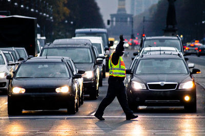 Traffic cop walking by illuminated cars on city street at dusk