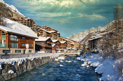 Buildings by river against sky during winter