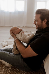 Side view of man holding baby at home