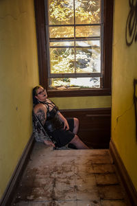 Young woman sitting on window in room