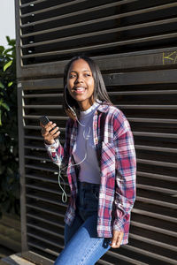 Portrait of smiling young woman holding smart phone while standing outdoors