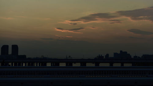 Silhouette bridge by buildings against sky at sunset