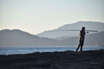 Man with fishing rod at beach against sky