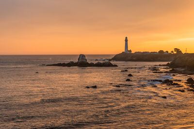 Lighthouse by sea against sky during sunset