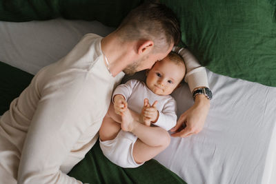 Young caucasian dad hugs his baby son in the bedroom, happy family