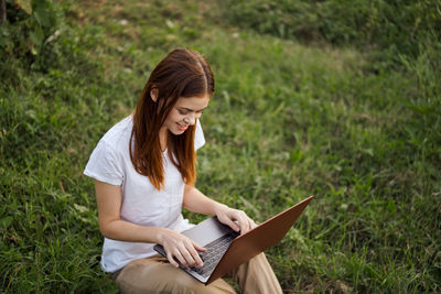 Young woman using phone while sitting on grass