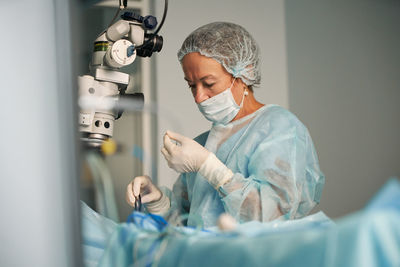 Adult female doctor in surgical uniform and sterile mask sitting in clinic