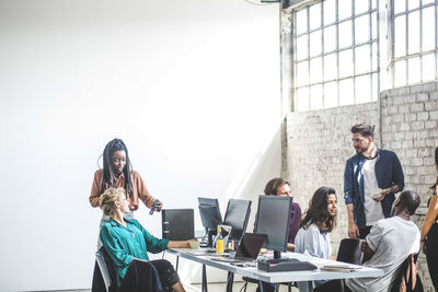 Businesswoman showing mobile phone to colleague while programmers discussing strategy in office