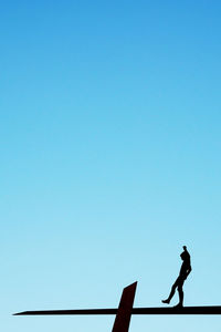 Side view of boy walking on silhouette platform against clear blue sky