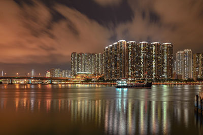 Illuminated buildings by sea against sky at night