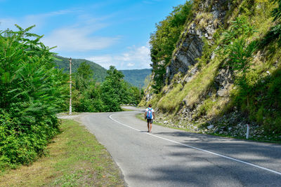 Rear view of man walking on road by mountain