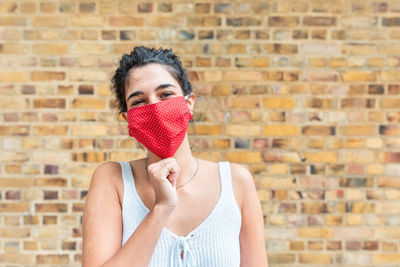 Portrait of woman wearing mask standing against brick wall