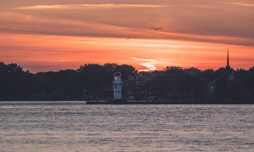 Silhouette of lighthosue by sea against orange sky