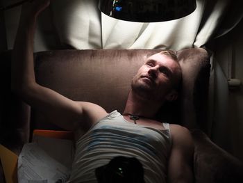 Young man holding illuminated lamp while sitting on armchair in darkroom