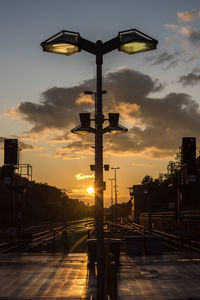 Silhouette street lights against sky during sunset