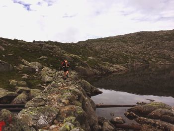 Mid distance view of female hiker hiking on rock formation by lake