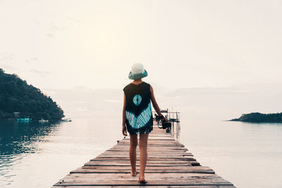 Rear view of woman standing on pier over lake against sky