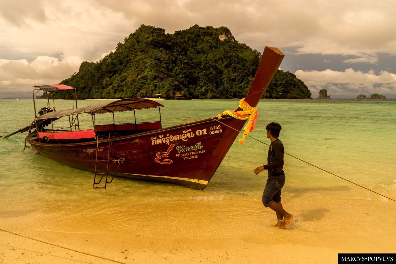 MAN ON BOAT MOORED AT BEACH