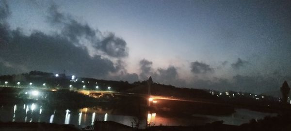 Illuminated bridge over river against sky in city at night