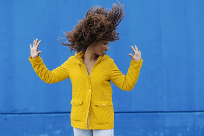 Woman with yellow umbrella standing against blue background