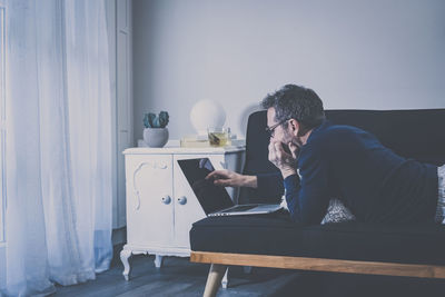 Man works with laptop sitting on the sofa. male home working in living room with remote office. 