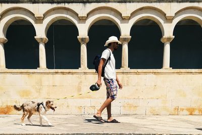 Side view of man with dog walking against built structure