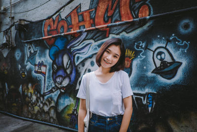 Portrait of smiling young woman standing against graffiti wall