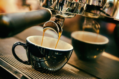 Close-up of espresso maker pouring coffee in cup on table at cafe