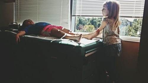 Girl looking at sister lying down on bed at hospital