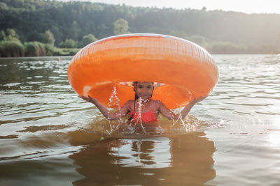 Girl has fun on big donut inflatable ring on lake on hot summer day, happy summertime, countryside