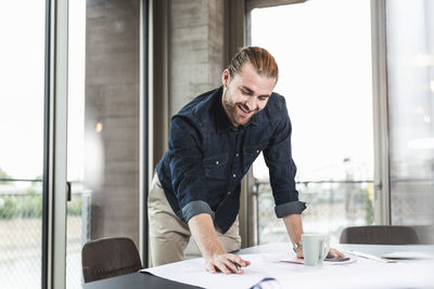 Smiling young businessman working on plan at desk in office