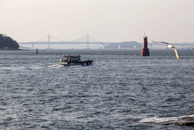 View of boat with lighthouse by bridge against clear sky