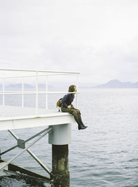 Woman sitting on pier while looking at river against clear sky