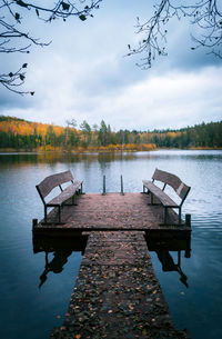 Empty bench by lake against sky