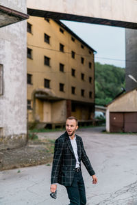 Young man looking away while standing on street against building in city