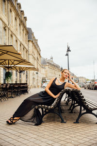 Portrait of confident young woman sitting on bench in city