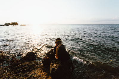 Man sitting on rock looking at sea against sky