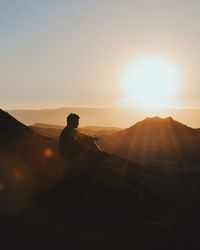 Silhouette of man sitting on landscape against sky