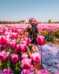 Woman sitting by pink flowers against sky