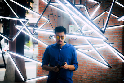 Portrait of man wearing sunglasses while standing against illuminated decoration