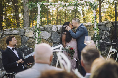 Newlywed couple kissing in front of guests and minister at wedding ceremony