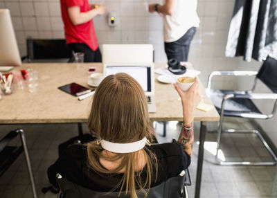 Rear view of young businesswoman having coffee with male colleagues in background at new office