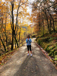 Full length of woman on road amidst trees during autumn